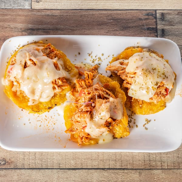 Three Cuban tostones topped with shredded chicken and melted cheese on a white plate.