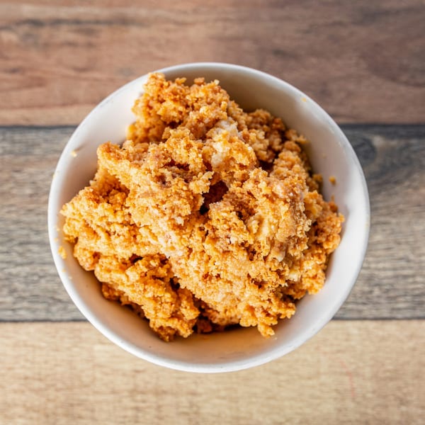 A white bowl filled with golden-brown, textured Cuban Gofio on a wooden table.