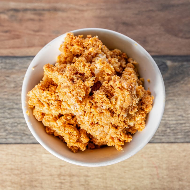 A white bowl filled with golden-brown, textured Cuban Gofio on a wooden table.