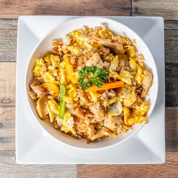 Cuban fried rice with chicken, scrambled eggs, and vegetables, garnished with parsley in a white bowl.