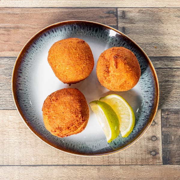 Three golden-brown Cuban croquettes and two lime wedges on a speckled plate.