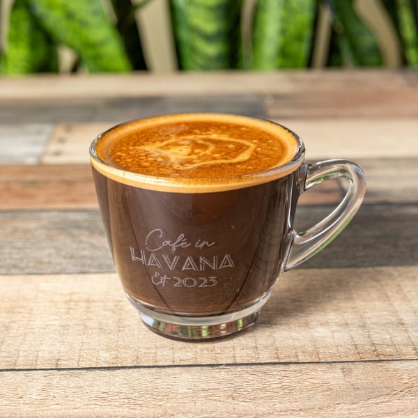A clear glass mug of Cuban coffee with "Café in Havana Est 2023" etched on it.