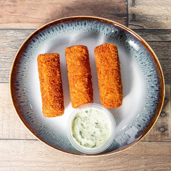 Three golden-brown Cuban croquettes on a white and blue plate with a side of green dipping sauce.